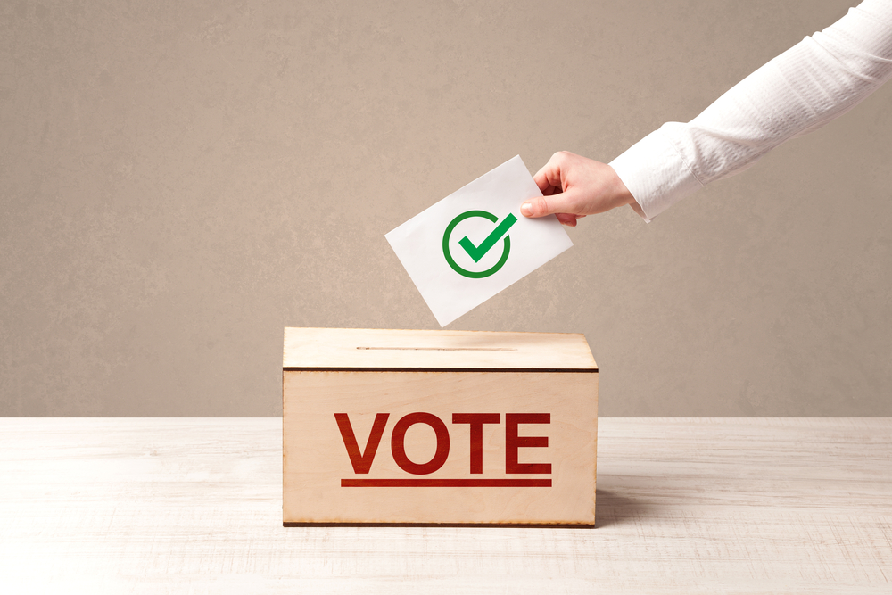 Close up of male hand putting vote into a ballot box, on grunge background